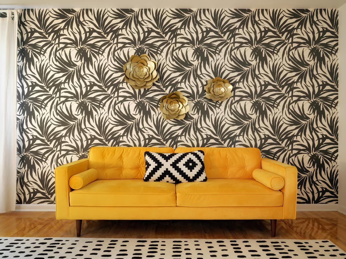 Mustard velvet sofa against black-and-white palm wallpaper with brass flower sculptures