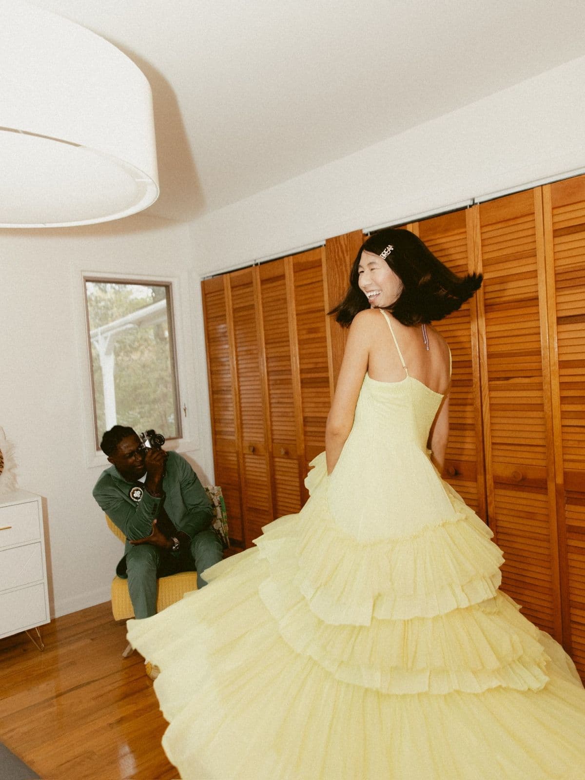 Model twirling a tiered yellow gown while a photographer shoots from a chair